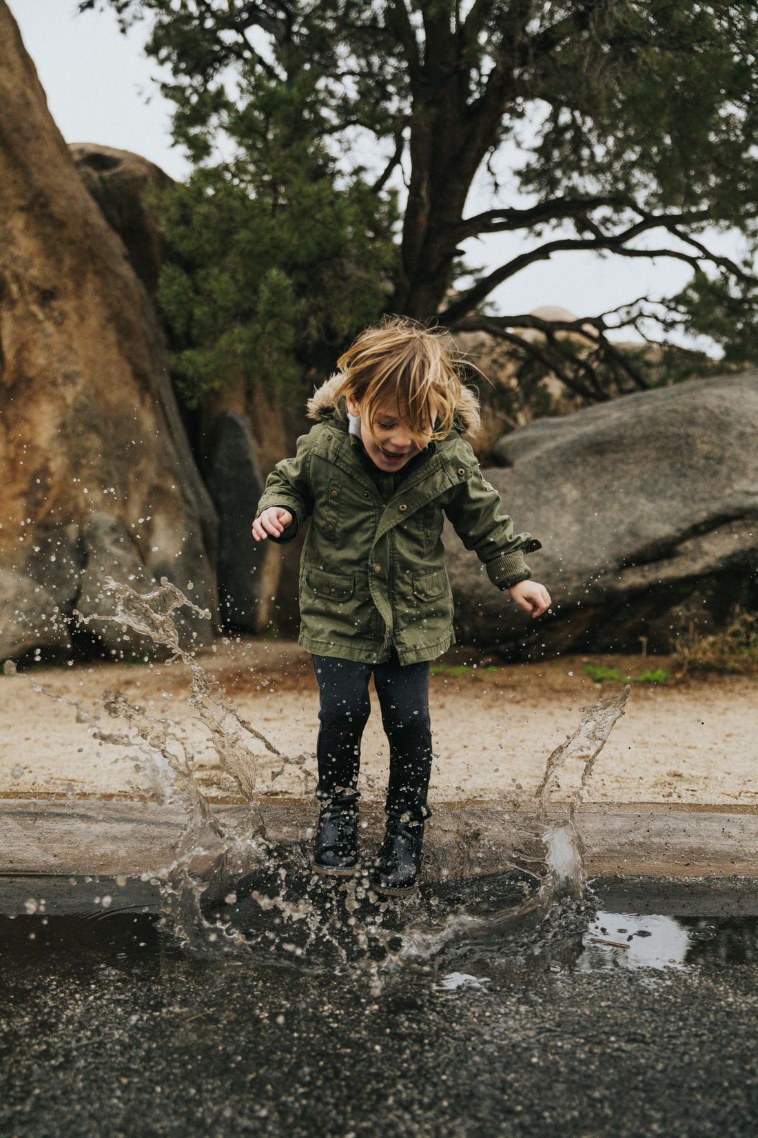 Enfant en ciré qui saute à pieds joints dans une flaque, en forêt